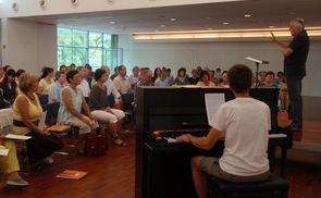 Josef Habringer (stehend) studiert mit 130 Sängerinnen und Sängern eine Woche lang Werke geistlicher Chormusik ein. Am Klavier: Korrepetitor Clemens Haudum. © Referat für Kirchenmusik der Diözese Linz.       